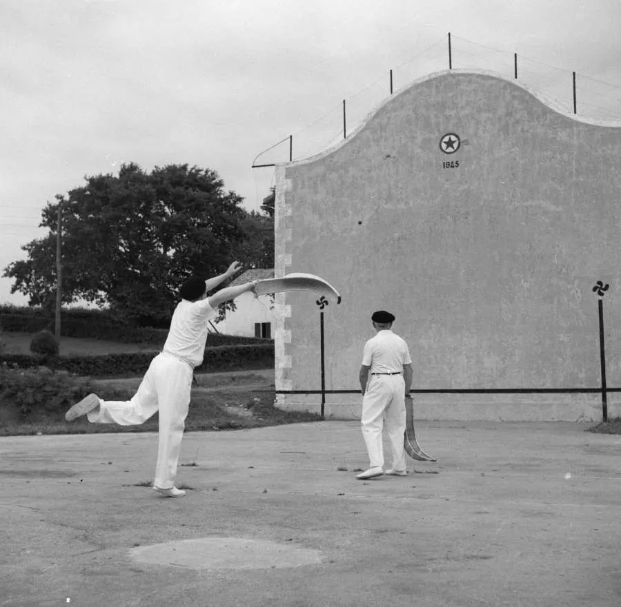 A cesta punta player swinging a long curved basket to throw the ball against the fronton wall