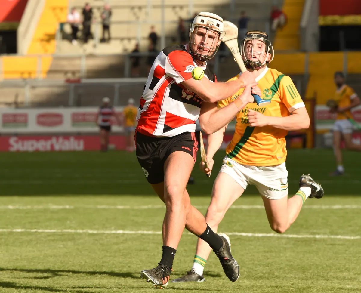 Two hurling players in helmets contesting the sliotar on a grass pitch, hurleys in hand