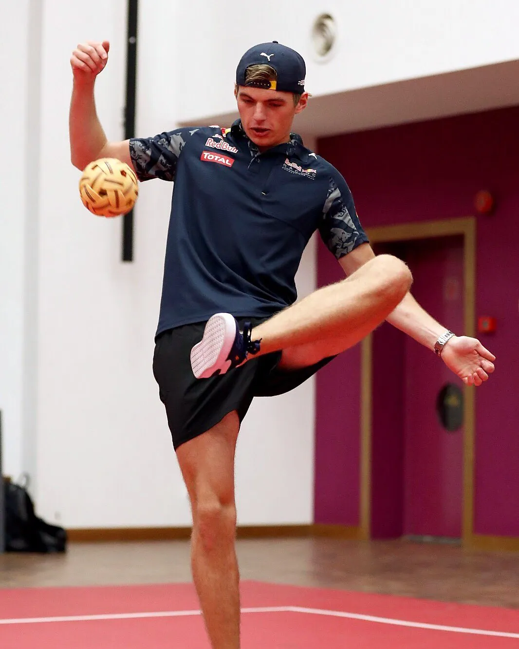 A sepak takraw player lifting a woven rattan ball with his foot on a red court